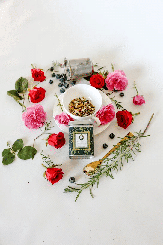 Premium loose leaf herbal tea in a green tea caddy and a white cup surrounded by red and pink roses