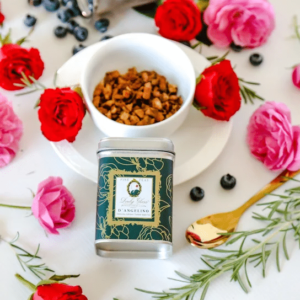 Premium Turkish Organic Apple Tea in a green tea caddy and white cup surrounded by red and pink roses, blueberries, and a golden spoon