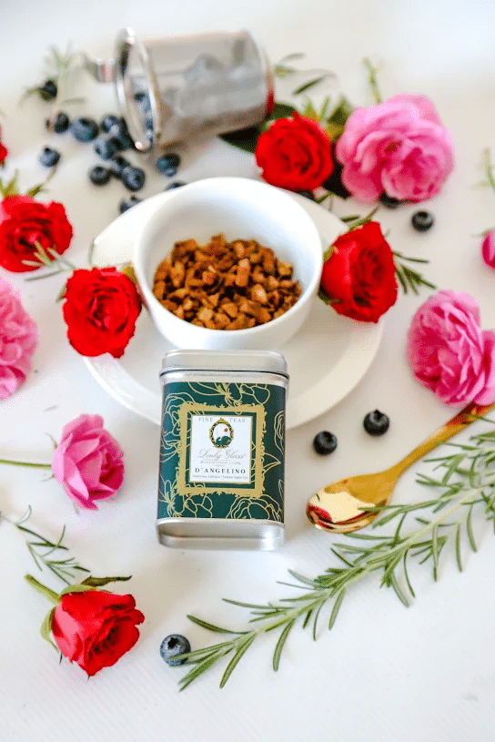 Premium Turkish Organic Apple Tea in a green tea caddy and white cup surrounded by red and pink roses, blueberries, and a golden spoon
