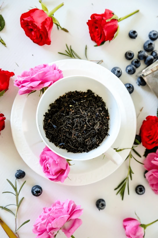 Premium loose leaf Earl Grey Blue Flower Tea in a green tea caddy surrounded by red roses