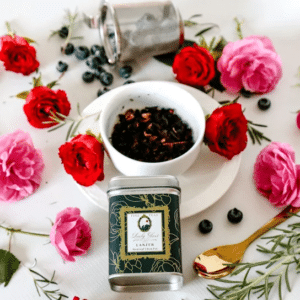 Premium fruit tea in a green tea caddy and a white cup surrounded by red and pink roses, blueberries, and a golden spoon
