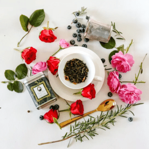 Premium loose leaf green tea in a green tea caddy and white cup surrounded by roses