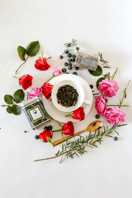Premium loose leaf green tea in a green tea caddy and white cup surrounded by roses