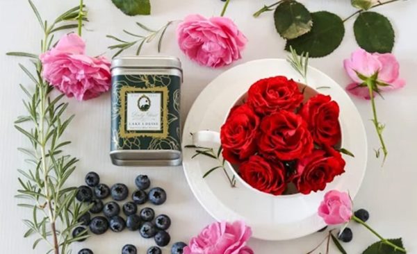 Premium loose leaf Earl Grey Blue Flower Tea in a green tea caddy surrounded by red roses